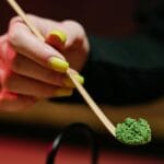 Dłoń trzymająca łyżeczkę z zielonym proszkiem matcha podczas ceremonii