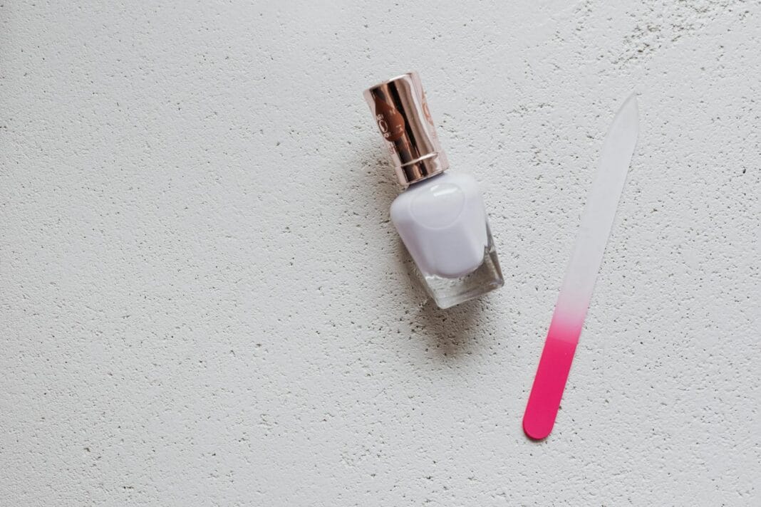 Biały lakier i różowy szklany pilnik do paznokci na białym tle