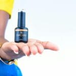 Dłoń kobiety trzymająca buteleczkę lakieru hybrydowego na jasnym tle