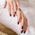 Dłoń kobiety z ciemnym manicure na tle spa, zadbane paznokcie i skórki