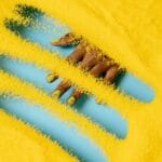 Dłoń z żółtym manicure częściowo zanurzona w żółtym pudrze