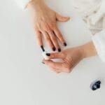 Kobieta w szlafroku maluje paznokcie ciemnym lakierem z góry