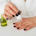 Kobieta w szlafroku nakłada serum pipetą na paznokcie dłoni