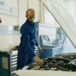 Mechanik w niebieskim kombinezonie sprawdza silnik auta w warsztacie