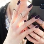 Dłoń kobiety z hybrydowym manicure i pierścionkami trzymająca smartfon