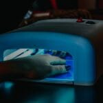 Dłoń z manicure hybrydowym utwardzana pod niebieską lampą LED