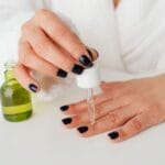 Kobieta w szlafroku nakłada pipetą serum na paznokcie dłoni