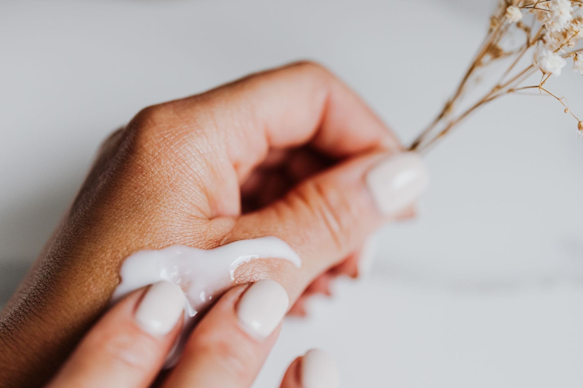 Dłonie nakładające krem z eleganckim manicure i suszonymi kwiatami