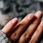 Dłonie kobiety w ciepłym swetrze z manicure żelowym i zdobieniami